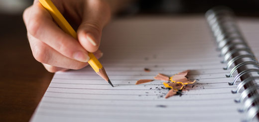 Notebook with hand holding pencil, pencil shavings next to the pencil and on the notebook