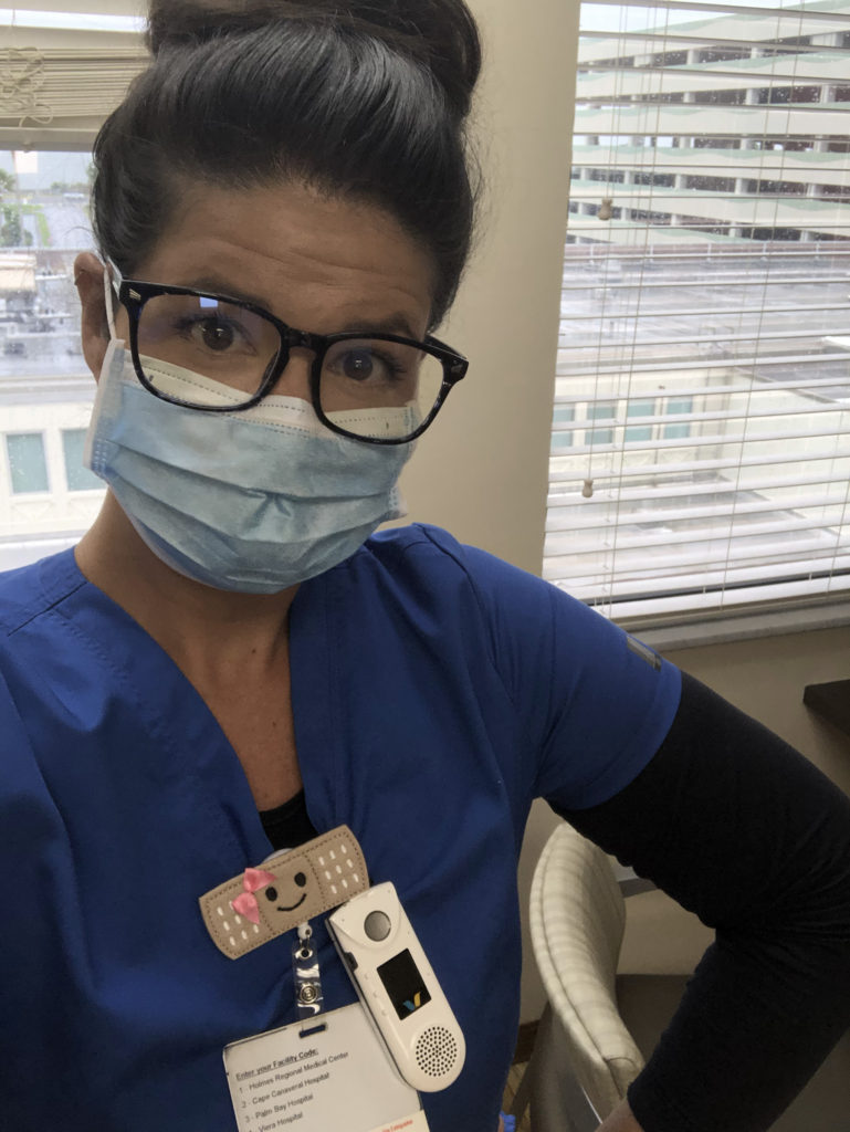 Woman (Spenser Streml) wearing blue scrubs and a face mask.