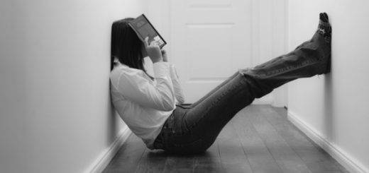 Person in hallway sitting on floor holding book up to their face with feet on the wall